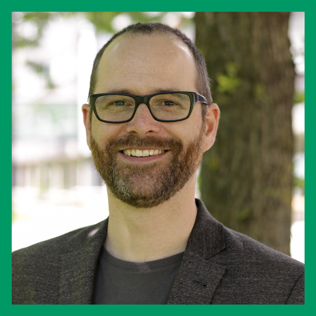 Portrait of Prof. Dr. Rupert Seidl. A white man in glasses smiles at the camera. He has short brown hair and a neatly trimmed beard and is wearing a grey blazer over a dark grey shirt.