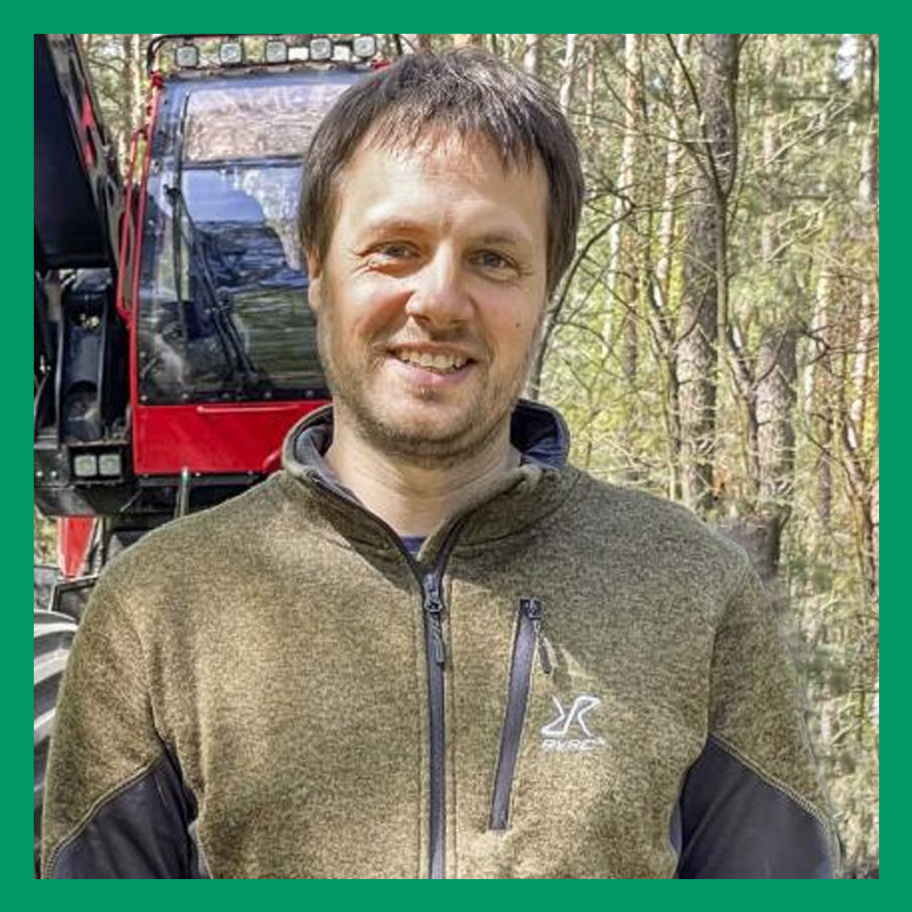 Portrait of Richard Georgi. A brown-haired man in a green zip-up sweater smiles at the camera. In the background is a forest.