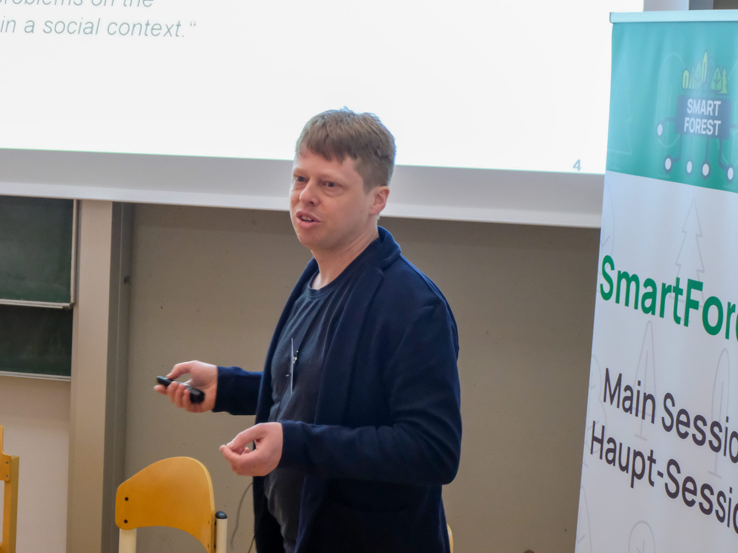 Prof. Dr. Fabian Faßnacht, a blond man wearing a blue shirt and jacket, lectures to the crowd at SmartForest 2025.