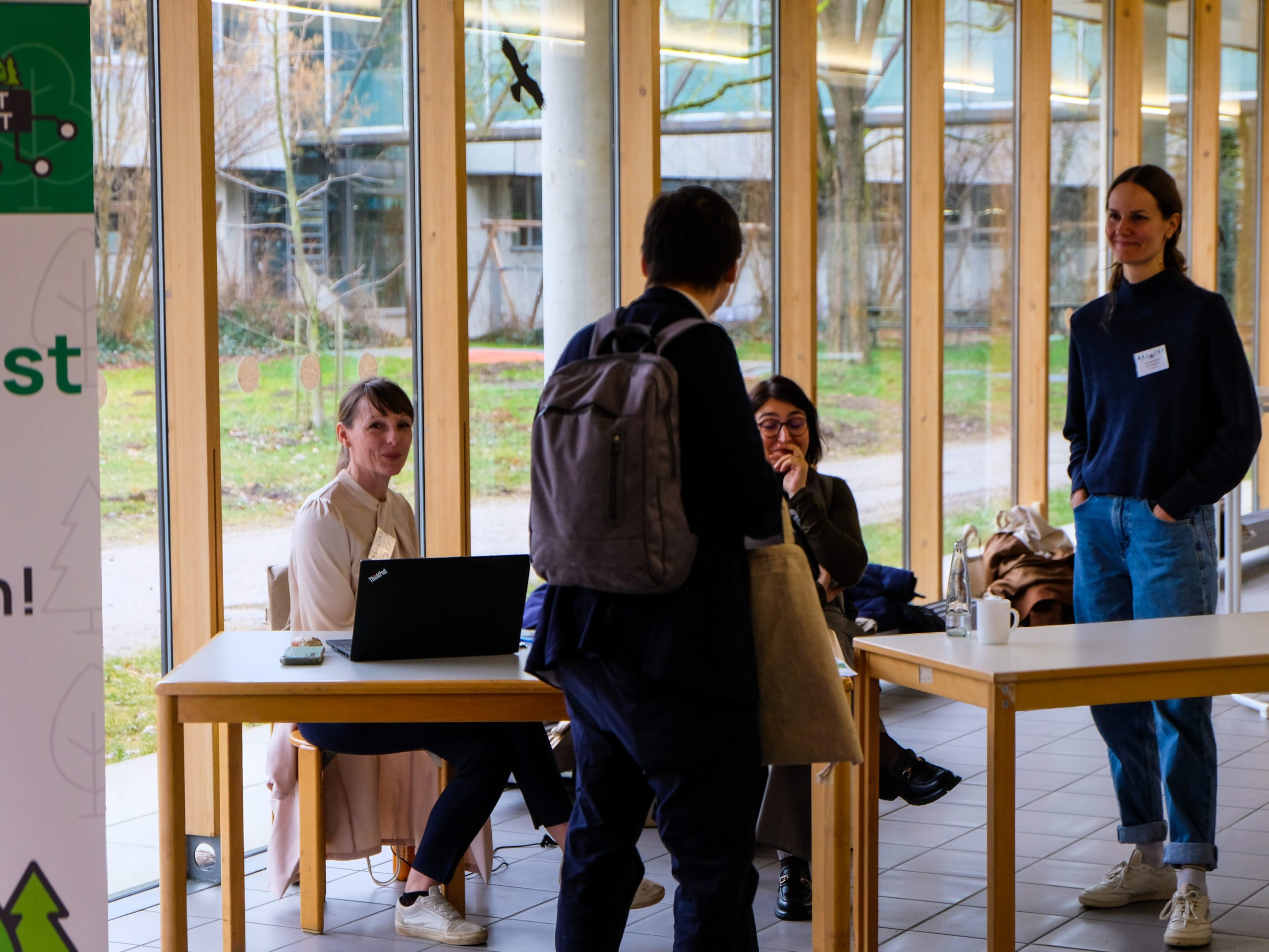 The SmartForest reception team, in this picture consisting of Franziska Hochenegger, Dr. Nina Krüger, and Anna Glissmann share a laugh with a dark-haired attendee carrying a backpack.