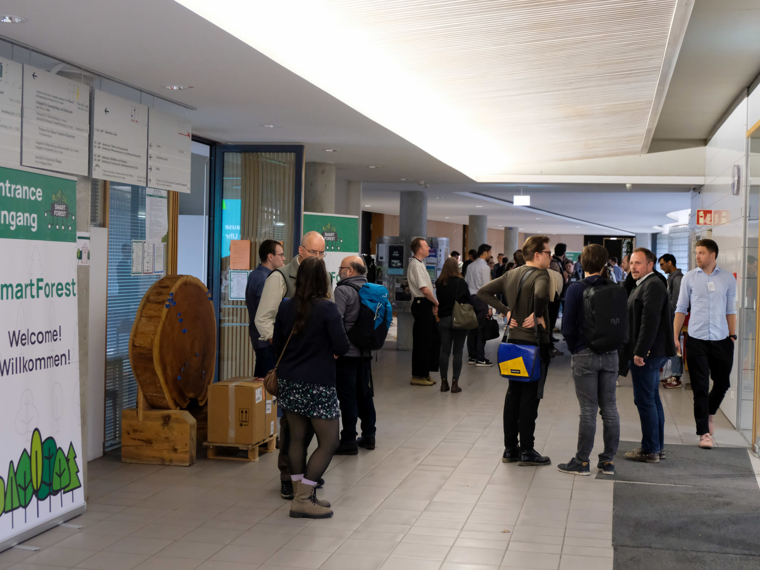 A shot of the entrance hall of SmartForest 2025 at the TU Munich in Freising, showing a large crowd broken up into smaller groups having friendly discussions.