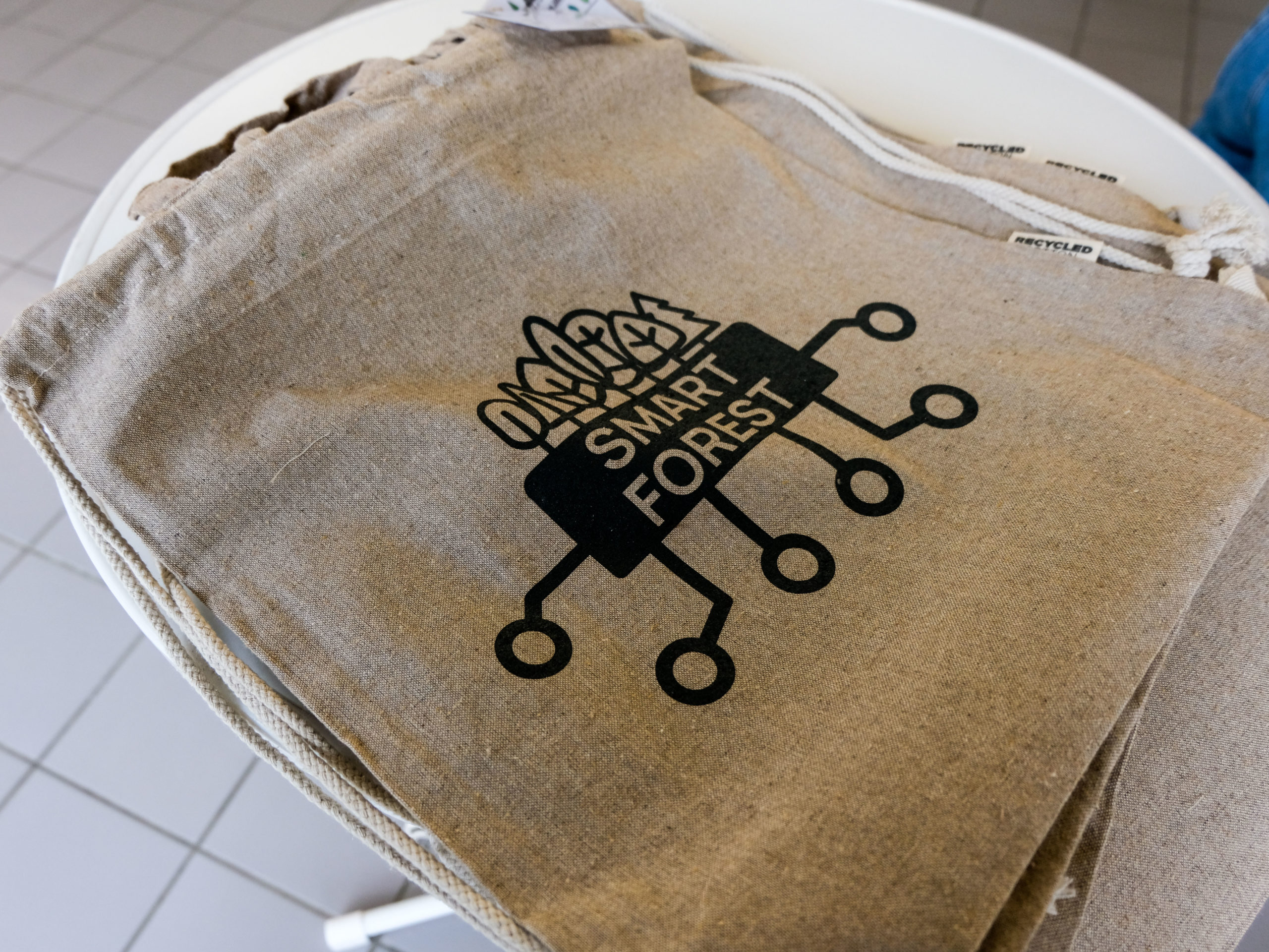 A stack of tan bags printed with the SmartForest-logo. A visible tag reads "Recycled cotton".