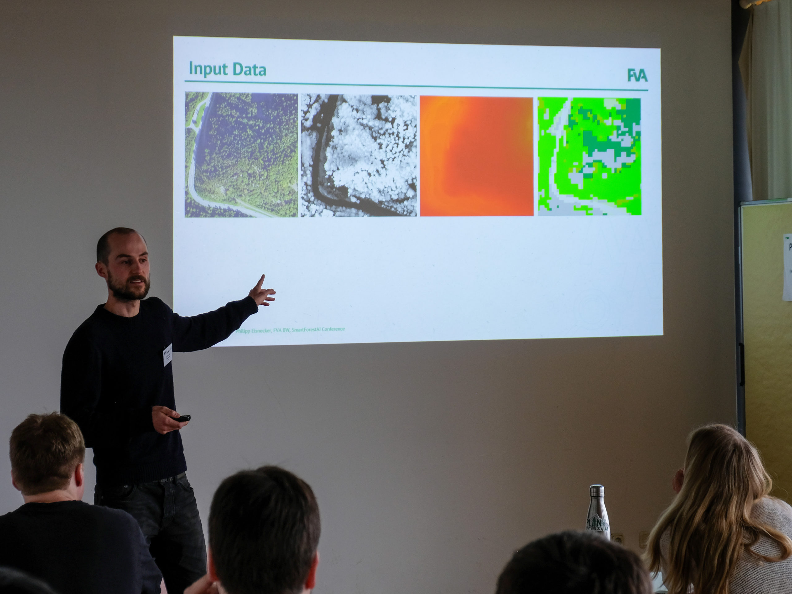 Philipp Eisnecker, a dark-haired man with a buzzcut and short beard, points at the projection of a slide with four pictures of the same aerial view of trees, each with different colours, titled "Input Data".