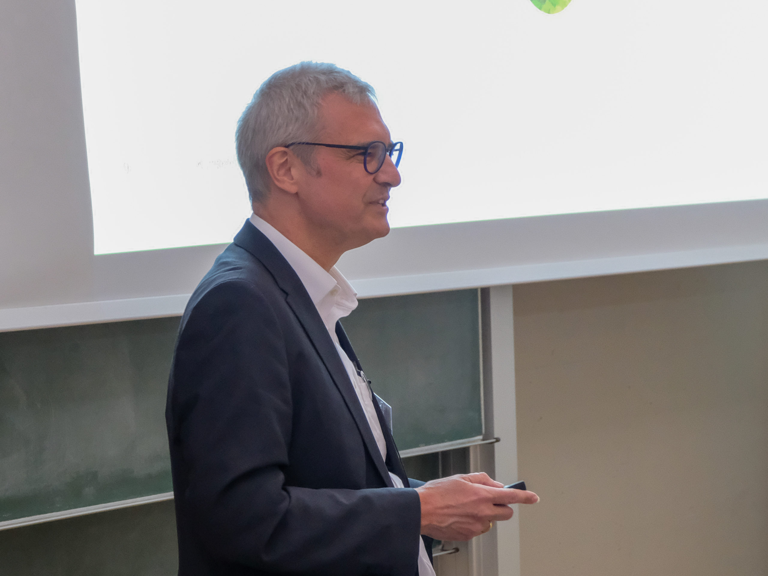 A grey-haired man in glasses and a smart suit addresses the crowd at SmartForest 2025.