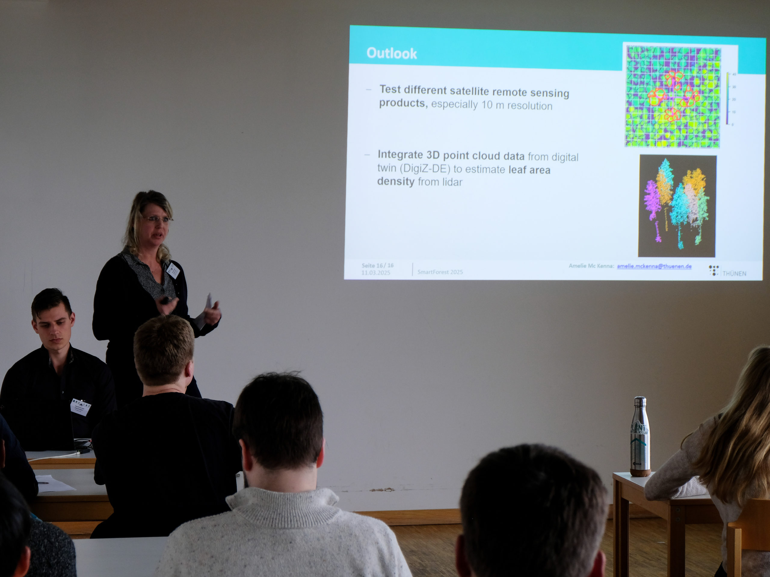 Amelie Mc Kenna, a blonde woman with small gold-rimmed glasses and a dark-coloured top, lectures to a classroom. Next to her is a projected slide with a picture showing a representation of tree crowns in green, yellow, and blue, with several circled in red, and another showing seven different clusters of coloured dots on a black background. The text besides these images reads: "Outlook. - Test different satellite remote sensing products, especially 10 m resolution, - Integrate 3D point cloud data from digital twin (DigiZ-DE) to estimate leaf area density from lidar"