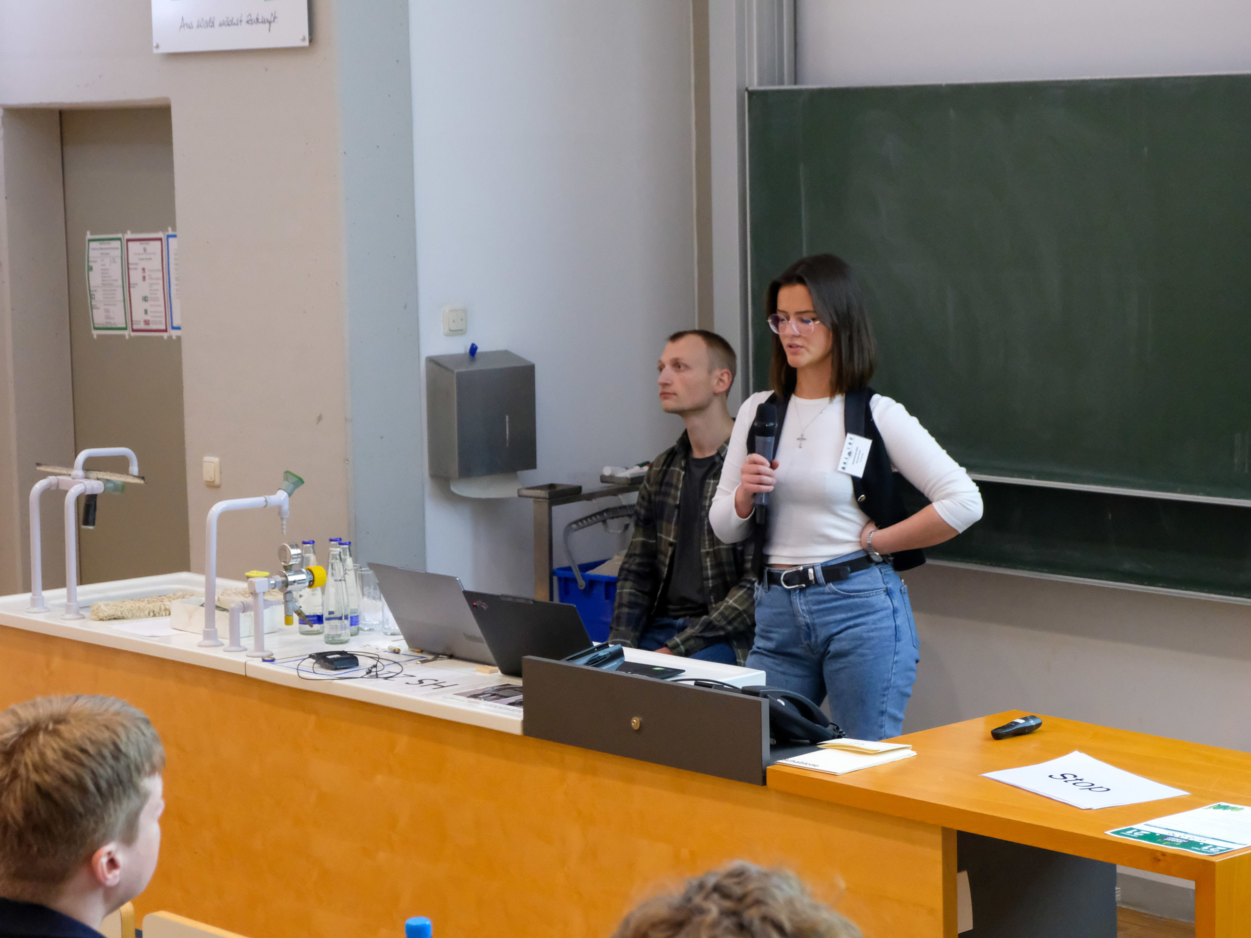 A dark-haired woman in glasses stands behind the lectern in the main SmartForest lecture hall, addressing the crowd.