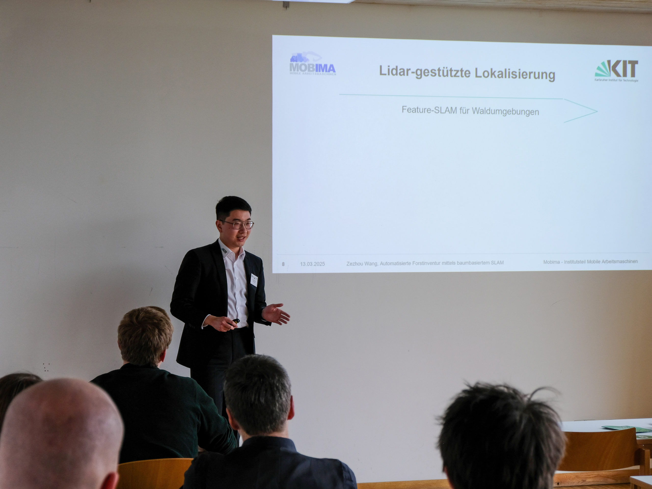 Zezhou Wang, a dark-haired Asian man in a smart suit and glasses, answers questions from the crowd at SmartForest 2025.