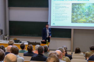 wetransform CEO Thorsten Reitz, a bearded man in a blue suit, addresses the crowd during his keynote at SmartForest 2026