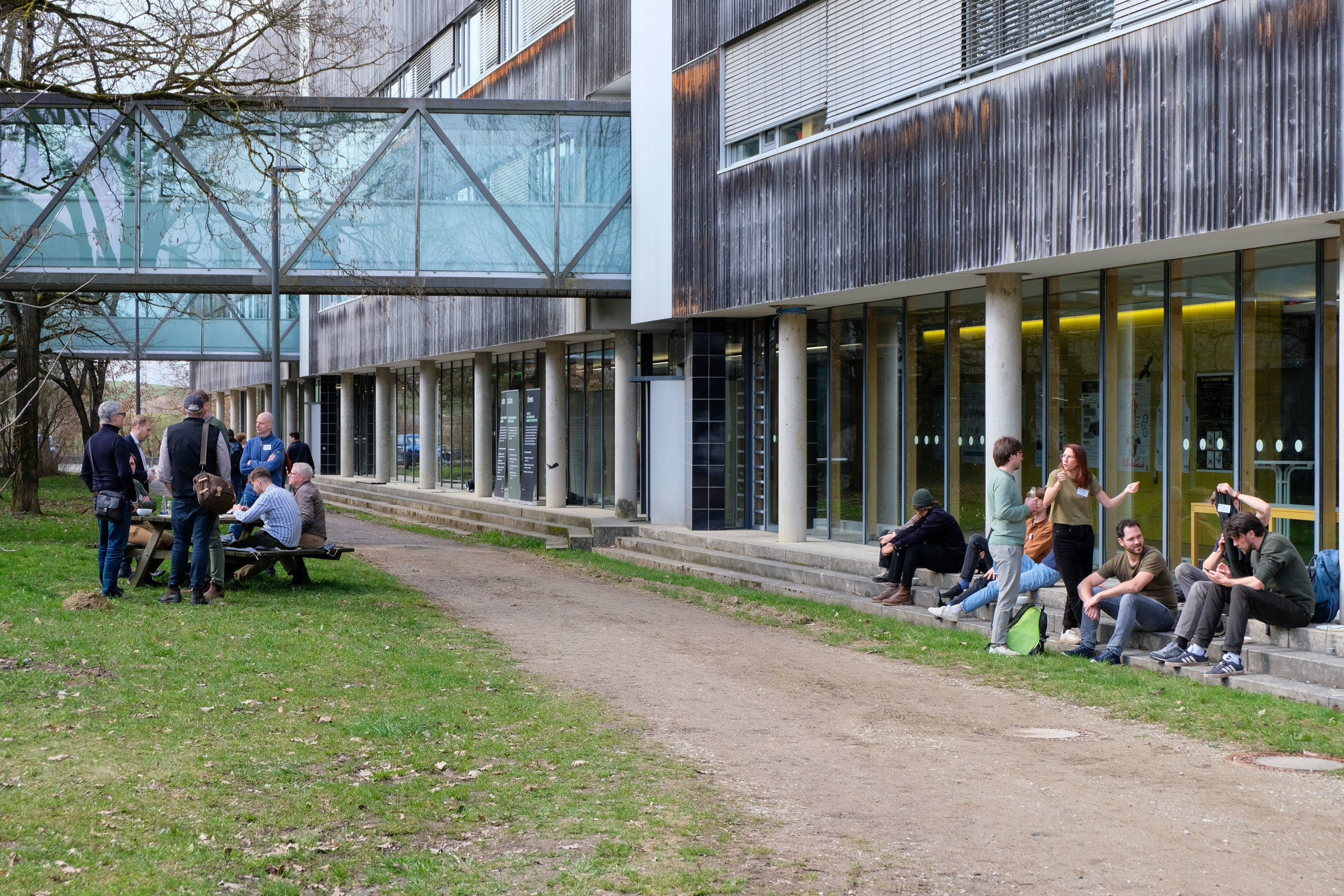 People sit on picnic benches and steps outside the TU Munich's building in Freising, engaged in various discussions during SmartForest 2026.
