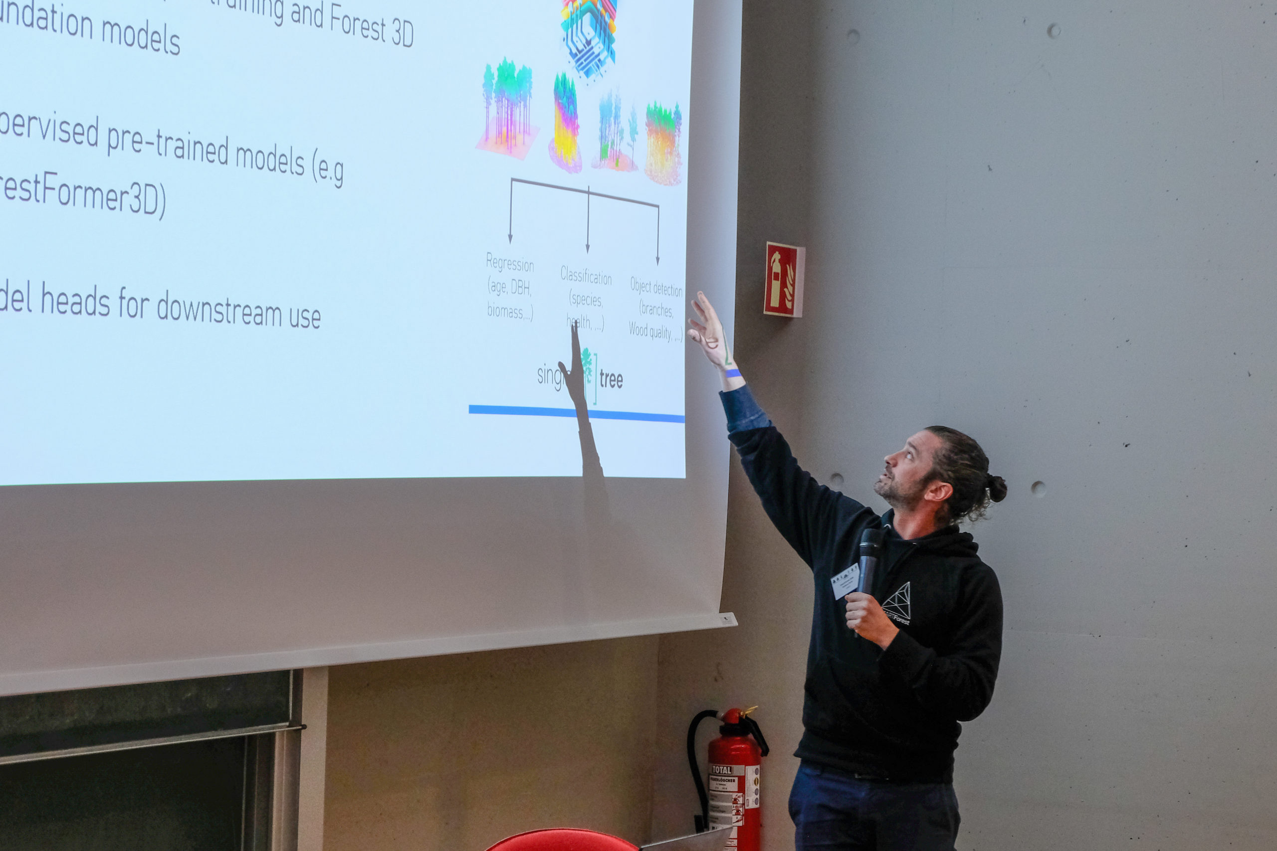 A SmartForest 2026 speaker reaches up towards the screen as he explains something.