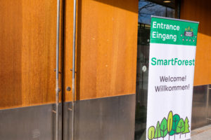 The entrance to SmartForest 2026. A SmartForest-branded roll-up banner stands beside large double doors to welcome guests to the conference on a sunny day.
