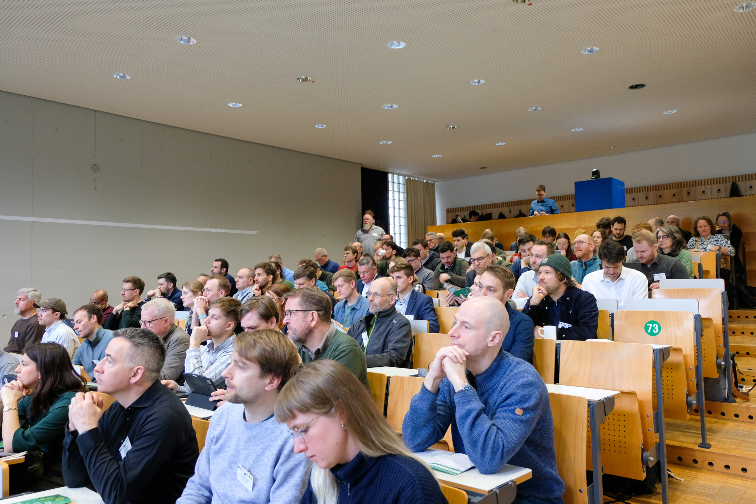 A crowd, dressed primarily in hues of green and grey, fills the seats of a lecture hall during SmartForest 2026.