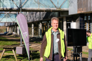 Martin Roth, forest manager in the Lake Constance district, smiles at the camera as he stands outdoors between a WOOD.IN.VISION banner and large television screen.