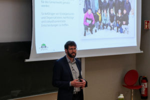 wetransform CEO Thorsten Reitz stands in front of a projected slide displaying a picture of the wetransform team, as well as the SmartForest logo