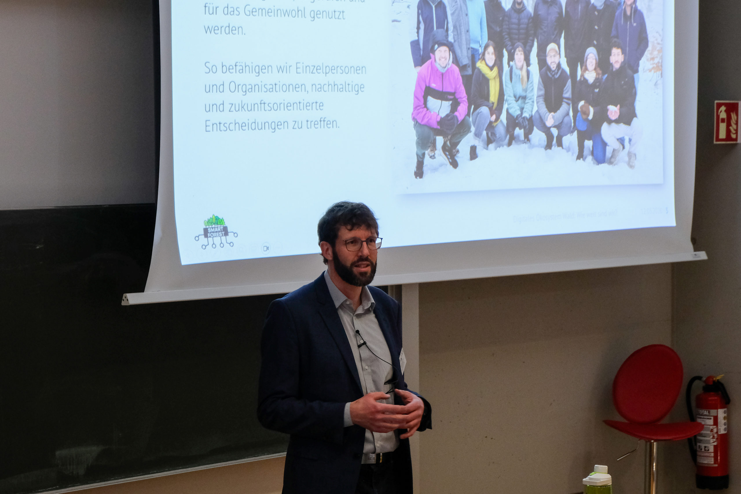 wetransform CEO Thorsten Reitz stands in front of a projected slide displaying a picture of the wetransform team, as well as the SmartForest logo