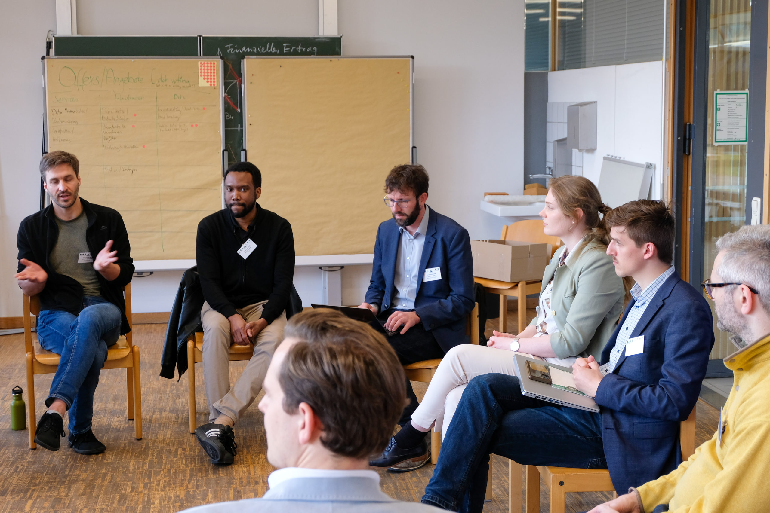 A SmartForest 2026 In-Depth Session. Part of a circle of people is visible, seated on wooden chairs in a classroom, engaged in discussion.
